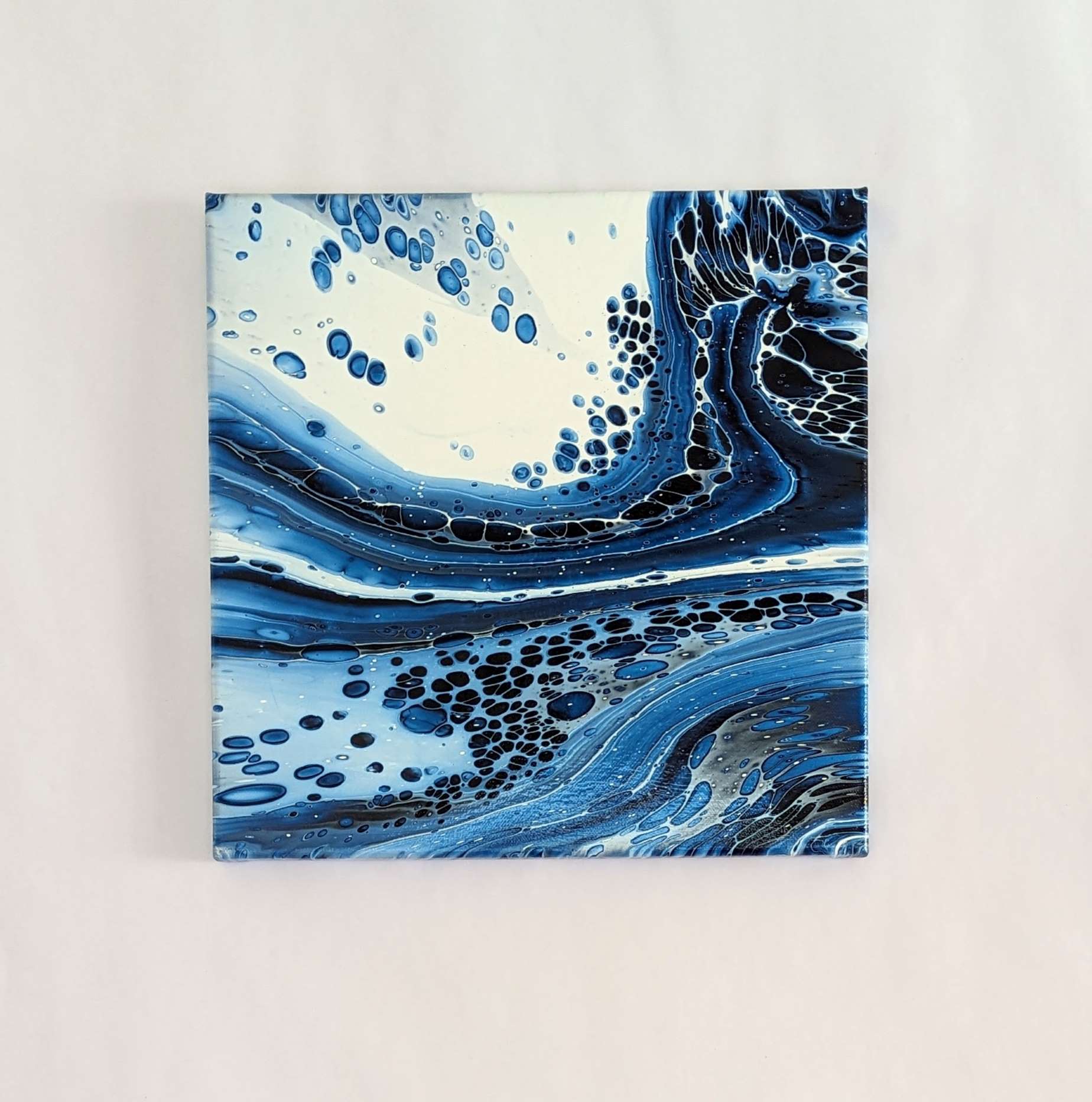 Canvas on wall – frontal view of original abstract painting. Made with professional grade acrylic paint: Prussian blue and white.