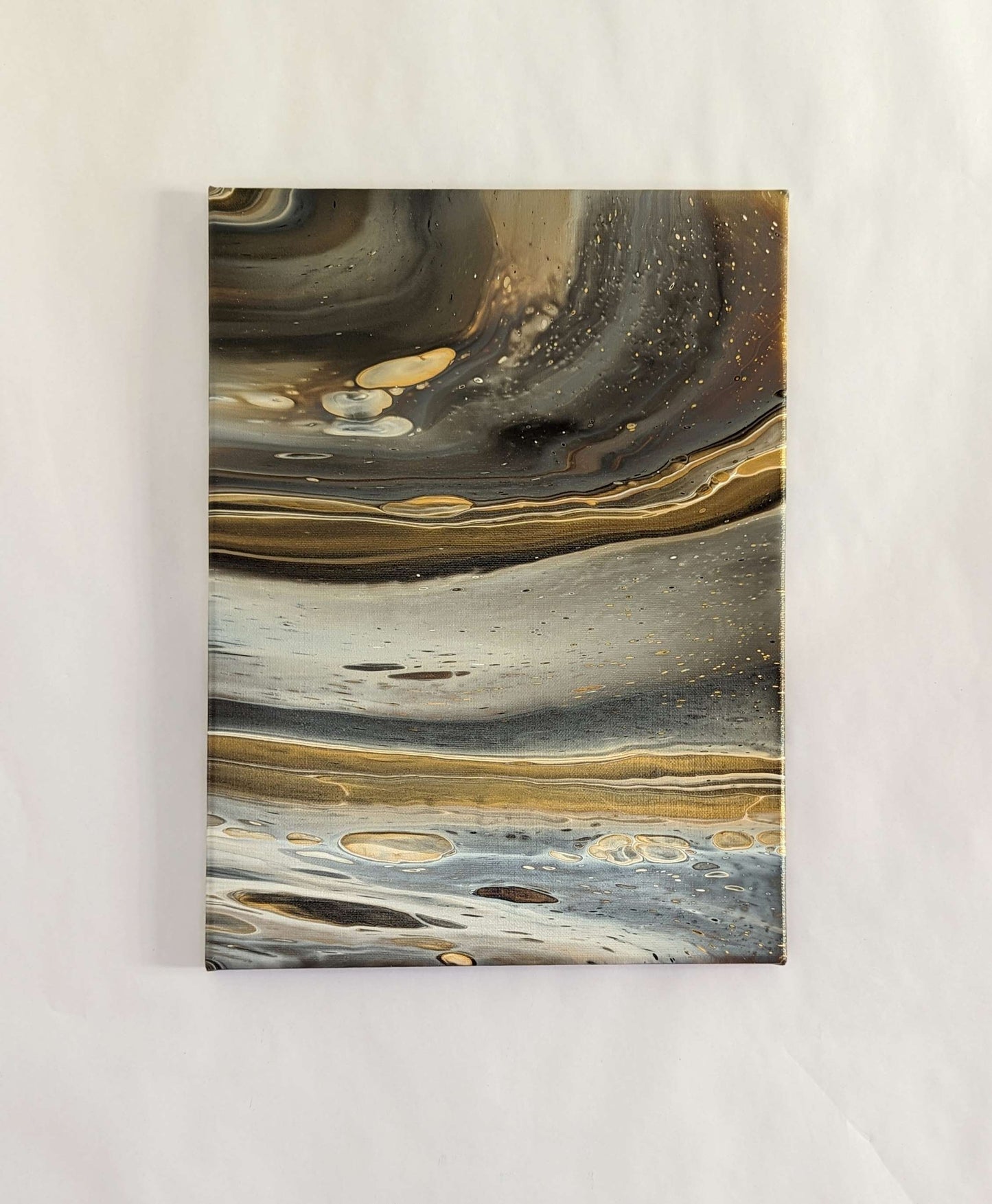 Canvas on wall – frontal view of original abstract painting in grey hues with gold made with professional grade acrylic paint.